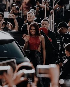 a woman waves to the crowd as she stands in front of a car