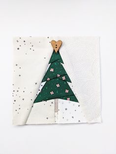 a piece of paper with a christmas tree cut out of it and a wooden heart on top