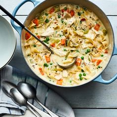 a pot filled with chicken noodle soup on top of a wooden table next to a spoon