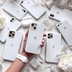 a person holding an iphone in front of five white cases on a table with flowers