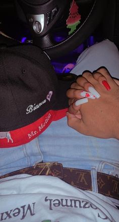 a person with red and white nail polish laying on their lap next to a baseball cap