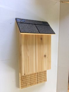 a wooden bird house hanging on the side of a white wall with a black roof