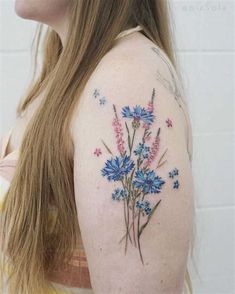 a woman's shoulder with blue flowers and butterflies on her left arm, in front of a white brick wall