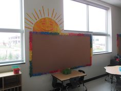 an empty classroom with desks and chairs in front of a bulletin board that has the sun drawn on it