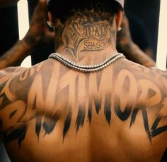 the back of a man with tattoos on his upper and lower half, wearing a baseball cap