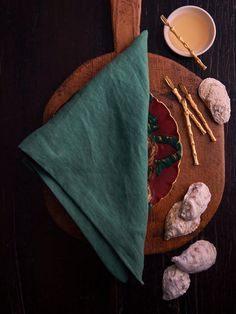 a wooden table topped with a green napkin next to cookies and a cup of tea