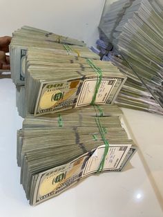 two stacks of money sitting next to each other on a white counter top in front of a person's hand