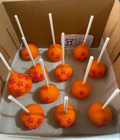 orange cake pops with pink sprinkles and white sticks in a cardboard box