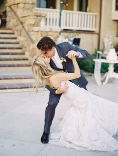 a bride and groom are dancing on the sidewalk outside their wedding venue in front of some stairs