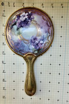 a mirror with flowers painted on it sitting on a piece of paper next to a ruler