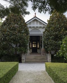 the front entrance to a white house surrounded by hedges