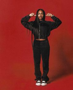 a woman standing in front of a red background with her hands on her head and arms behind her head