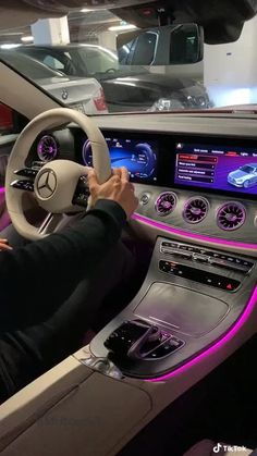 a man driving a car with purple lights on the dash and steering wheel, in front of other cars