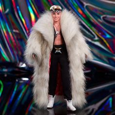 a barbie doll wearing a white fur coat and black pants on a stage with colorful lights in the background