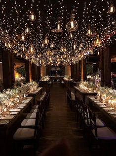 a long dining room with lights strung from the ceiling and tables covered in white linens