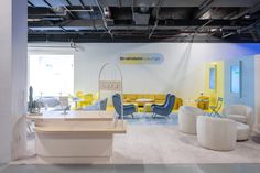 the interior of an office with yellow and blue chairs, white tables and couches