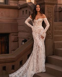 a woman standing on some steps wearing a dress with long sleeves and an off the shoulder design