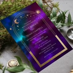 a purple and blue wedding card on top of a table next to some greenery