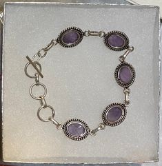 This eight inch artistically handcrafted Amethyst bracelet would be a perfect gift or addition to your own collection! Each Amethyst measures approximately 1/2 inch in full length! The metal is silver plated. An 8-inch Amethyst Gemstone Bracelet is a stunning accessory that can add elegance and sophistication to any outfit.  This bracelet features natural amethyst stones that have a rich purple hue and a smooth texture.  Amethyst is known as a stone of spirituality, intuition, and peace. It can Silver Oval Amethyst Bracelets, Handmade Amethyst Sterling Silver Bracelet, Handmade Sterling Silver Amethyst Bracelet, Handmade Sterling Silver Round Amethyst Bracelet, Silver Bracelet With Amethyst Natural Stones, Silver Amethyst Bracelets With Natural Stones, Silver Amethyst Bracelet With Natural Stones, Nickel-free Amethyst Bracelet, Handmade Adjustable Amethyst Sterling Silver Bracelet