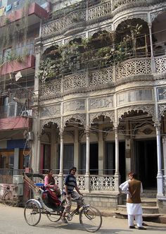 two people are riding on a bicycle in front of an old building with balconies