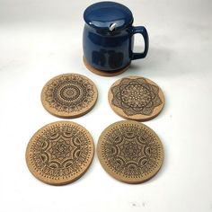 four coasters with designs on them sitting next to a blue coffee cup and saucer