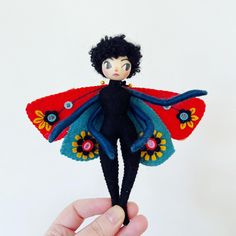 a hand holding a small doll in the shape of a fairy with black hair and blue eyes