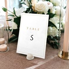 the table numbers are displayed on top of a card and surrounded by candles, flowers, and glass vases