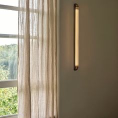 a light that is on the side of a wall next to a window with sheer curtains