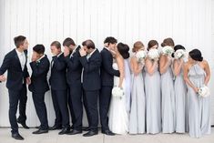 a group of people standing next to each other in front of a white wall wearing suits and ties