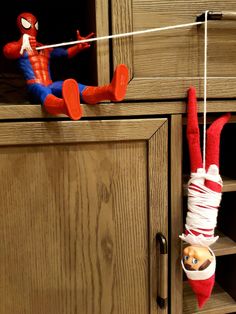 a spiderman toy hanging from the side of a wooden cabinet next to an elf's hat