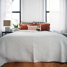 a bed with white and orange comforter in a bedroom next to two lamps on either side of the bed