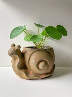 a small ceramic planter with a snail on it's side and a green plant in the middle