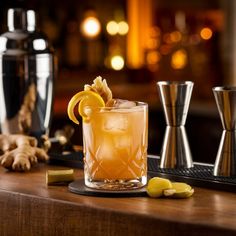 a glass filled with lemonade sitting on top of a table next to two cocktail shakers