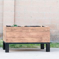 a wooden planter sitting on top of a sidewalk next to a brick wall and grass