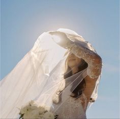 a woman in a wedding dress holding a veil over her head