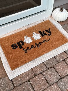 a door mat that says spooky season on it next to a white pumpkin