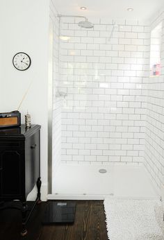 a white tiled bathroom with a black cabinet and clock on the wall next to it