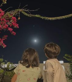 two children are looking at the moon in the night sky with pink flowers hanging over them