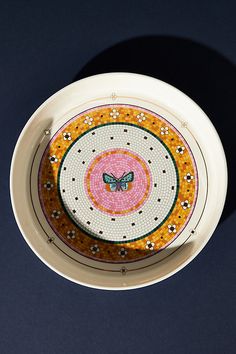 a white plate with a butterfly painted on the front and side, sitting on a black surface