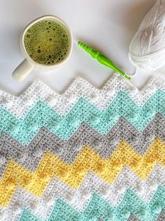 a crocheted blanket next to a ball of yarn and a green knitting needle