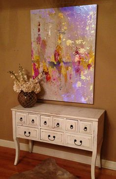 a painting is hanging on the wall next to a white dresser with drawers and flowers