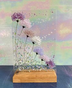 a glass vase filled with flowers on top of a wooden stand next to a wall