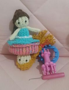 a crocheted doll sitting on top of a basket next to a sewing needle