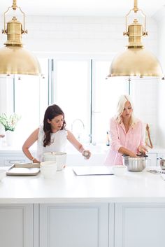 two women preparing food in a kitchen with gold pendant lights over the sink and counter tops