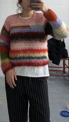 a woman taking a selfie in front of a mirror wearing striped sweater and black pants