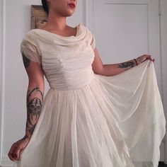 a woman in a white dress is holding onto a piece of cloth with tattoos on her arm