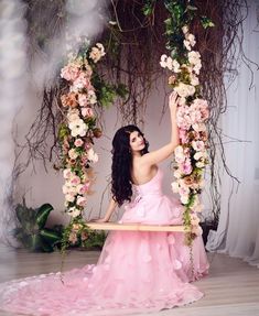 a woman in a pink dress is sitting on a swing with flowers around her neck