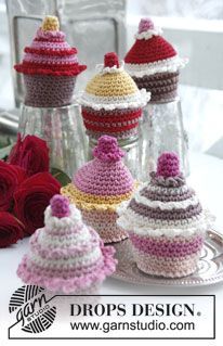 crocheted cupcakes are displayed in glass vases with red roses behind them