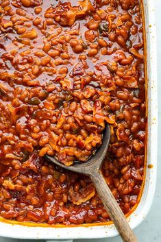 baked beans in a white casserole dish with a wooden spoon resting on top