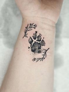 a small paw print on the wrist with leaves and flowers around it in black ink